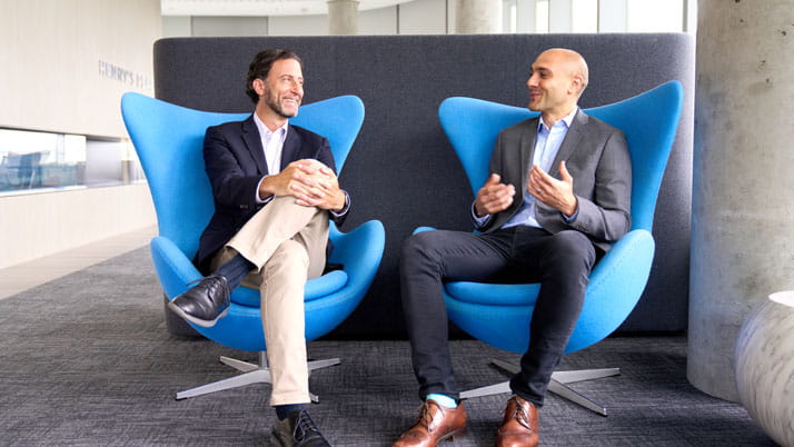 Two men dressed in business casual attire sitting in chairs.