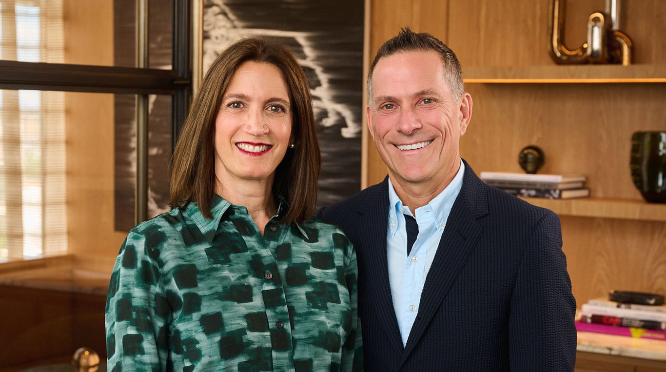 A woman with brown shoulder-length hair standing next to a man wearing a blue collared shirt and sport coat.