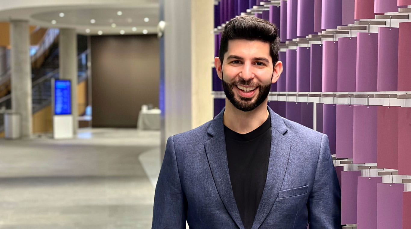 A man with a beard wearing a sport coat and standing next to a colorful wall
