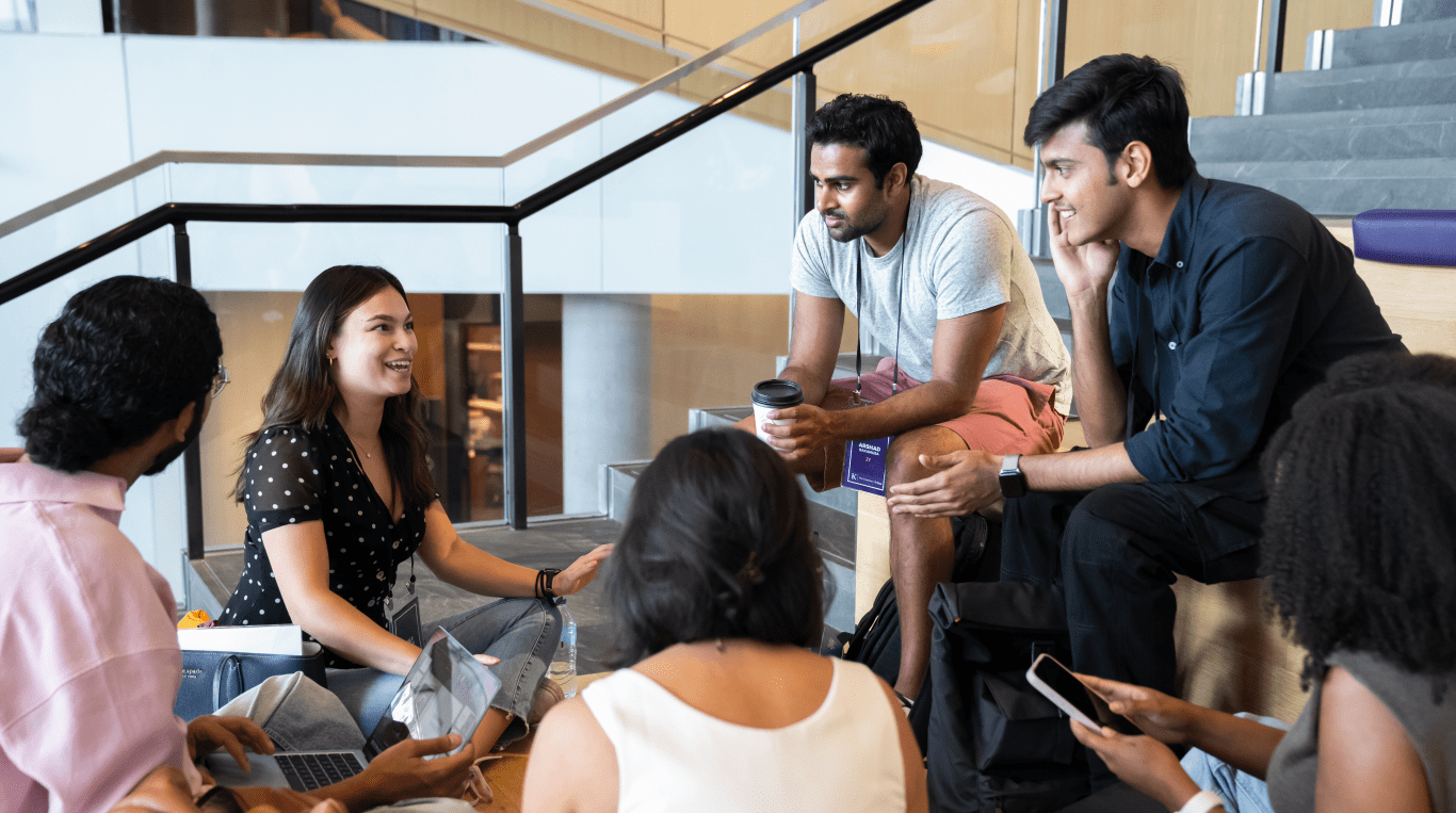 A group of new MBA students sit on stairs at the Global Hub