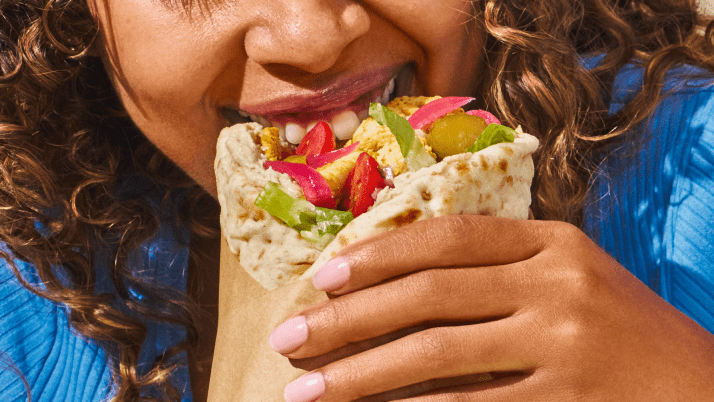 A woman with curly brown hair biting into a wrap