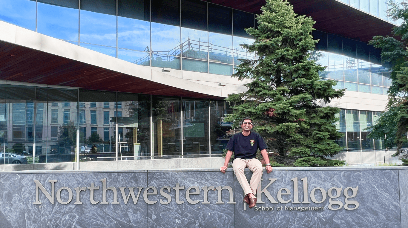 A Kellogg Full-Time MBA student sitting atop of the school's signage posing for a pic