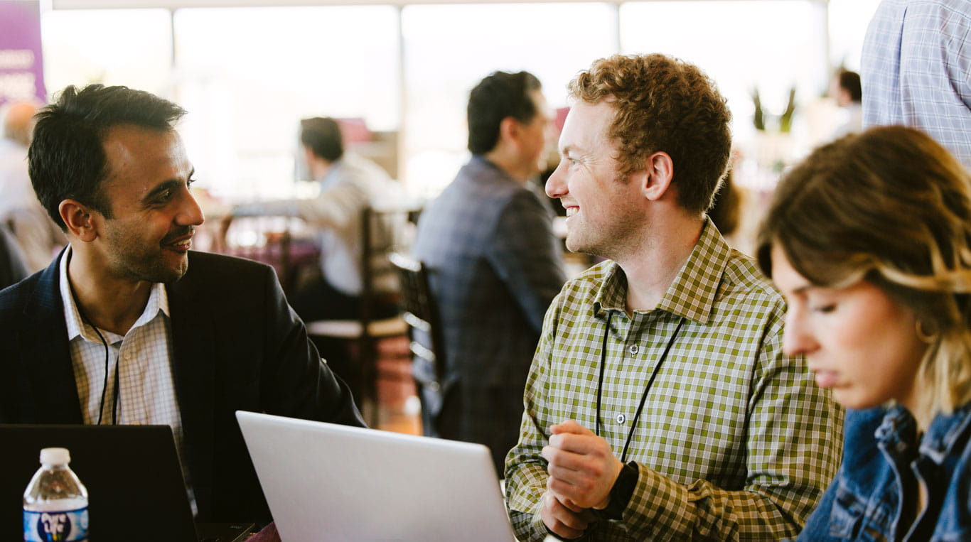 A woman sitting next to two men who are sitting in front of a laptop and talking with one another.
