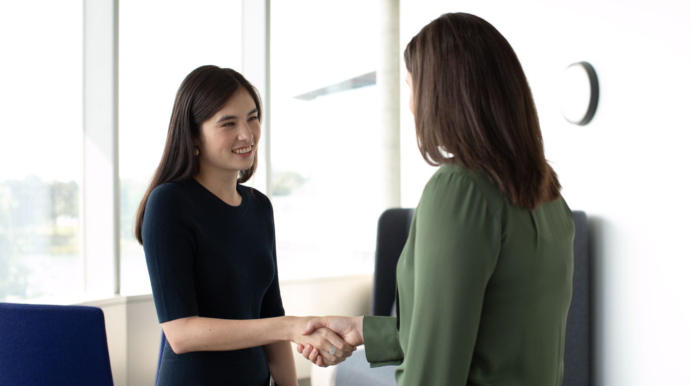 A woman wearing a green blouse shaking hands with another woman who is wearing a dark blouse.