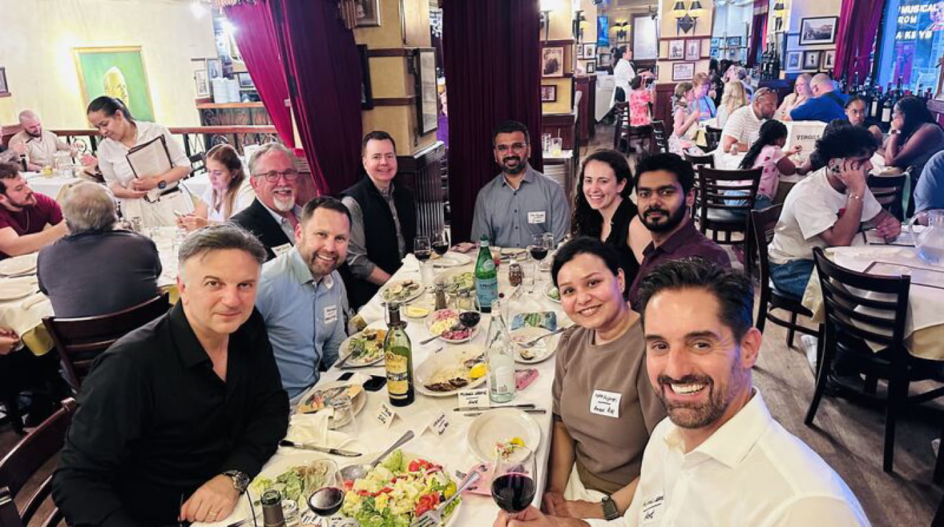 A smiling group of men and women eating dinner at a restaurant.