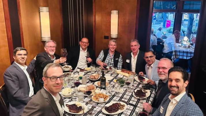 A group of men wearing blazers sitting around a dinner table at a restaurant