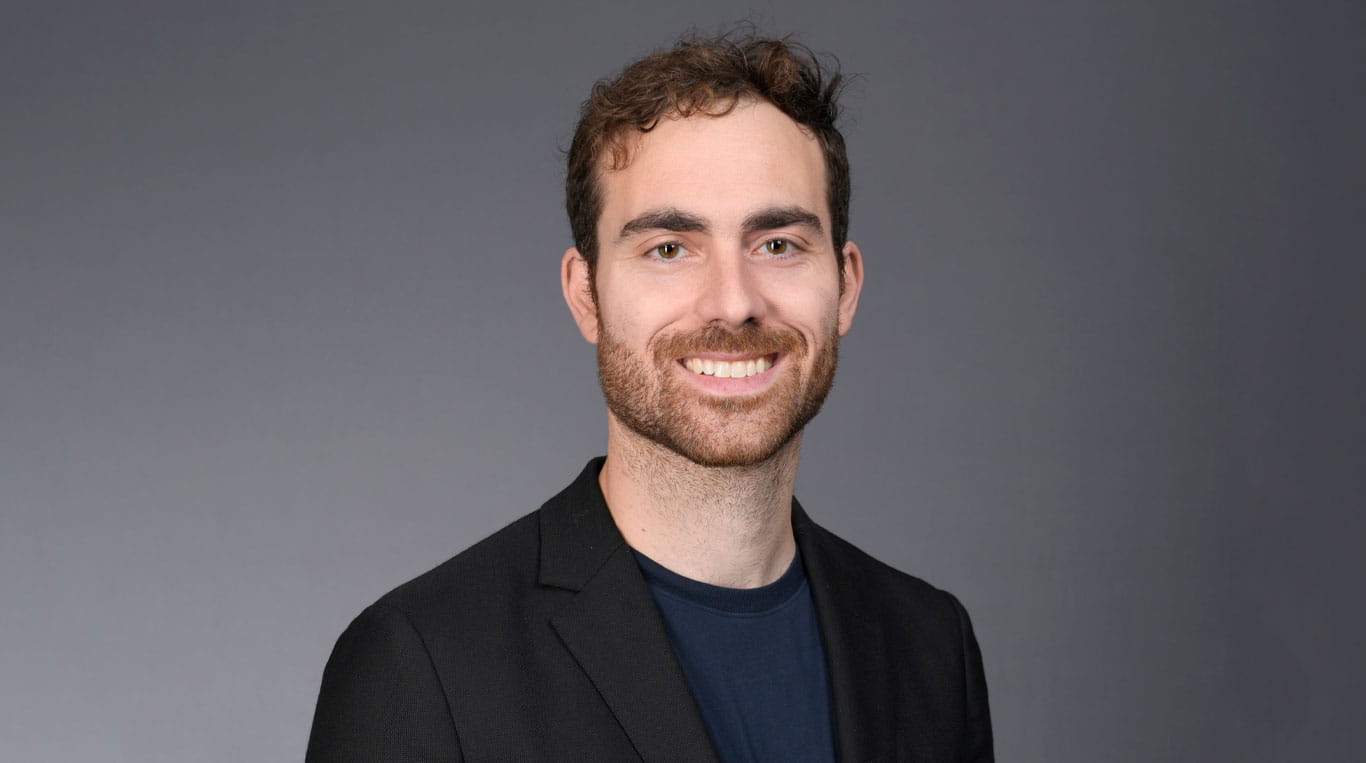 A smiling man with a beard wearing a dark blazer 