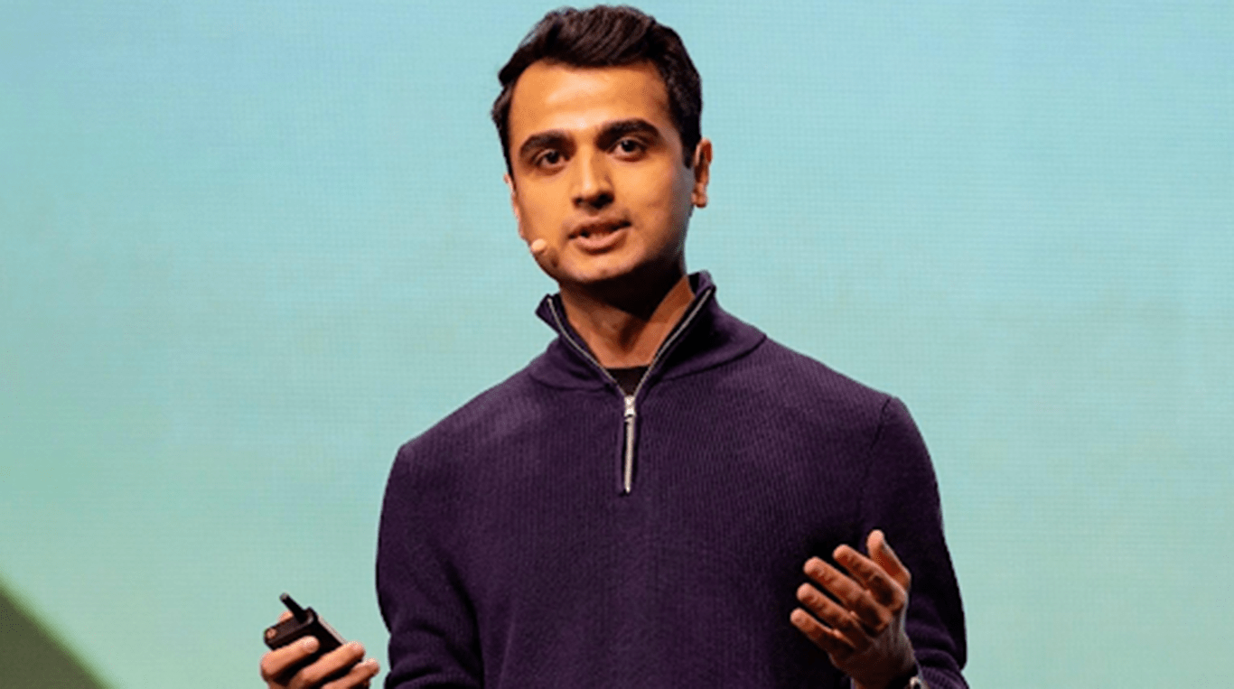 A man wearing a headset mic and dark clothing with arms bent at his side