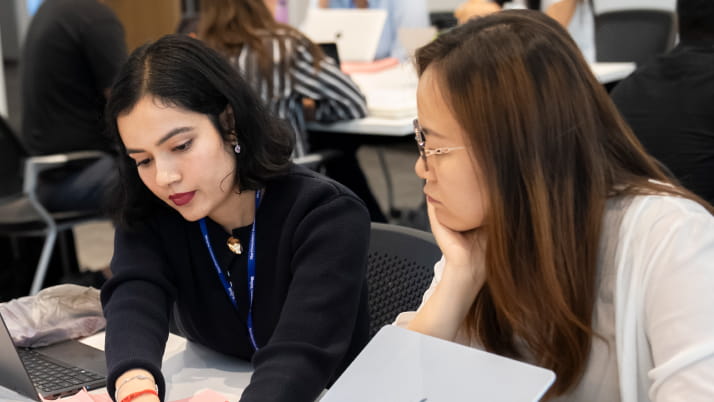 two women sitting at a table, looking through documents and information 
