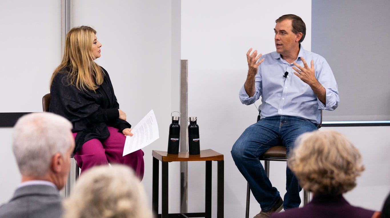 A man and a woman sitting on stools in front of a crowd