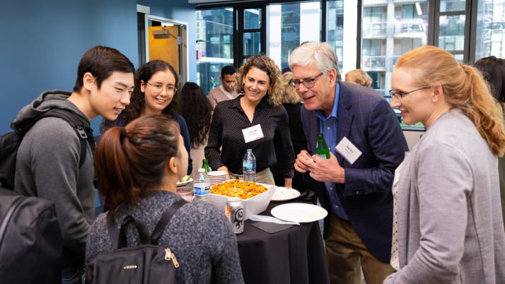 A group of people gathered around a man wearing a blazer and glasses