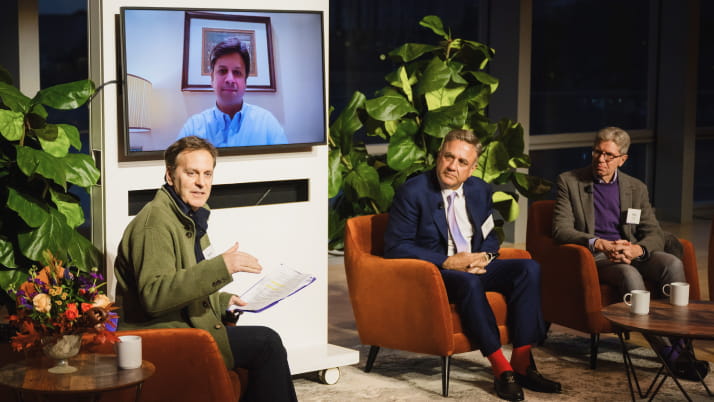 Three men sitting in brown chairs with plants and a tv in the background