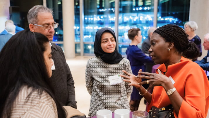 A Black woman wearing an orange scarf talking with two women and a man wearing glasses