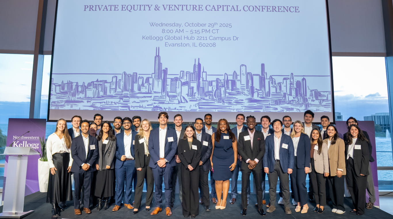 A group of men and women in professional attire standing in front of a projector screen on a stage.