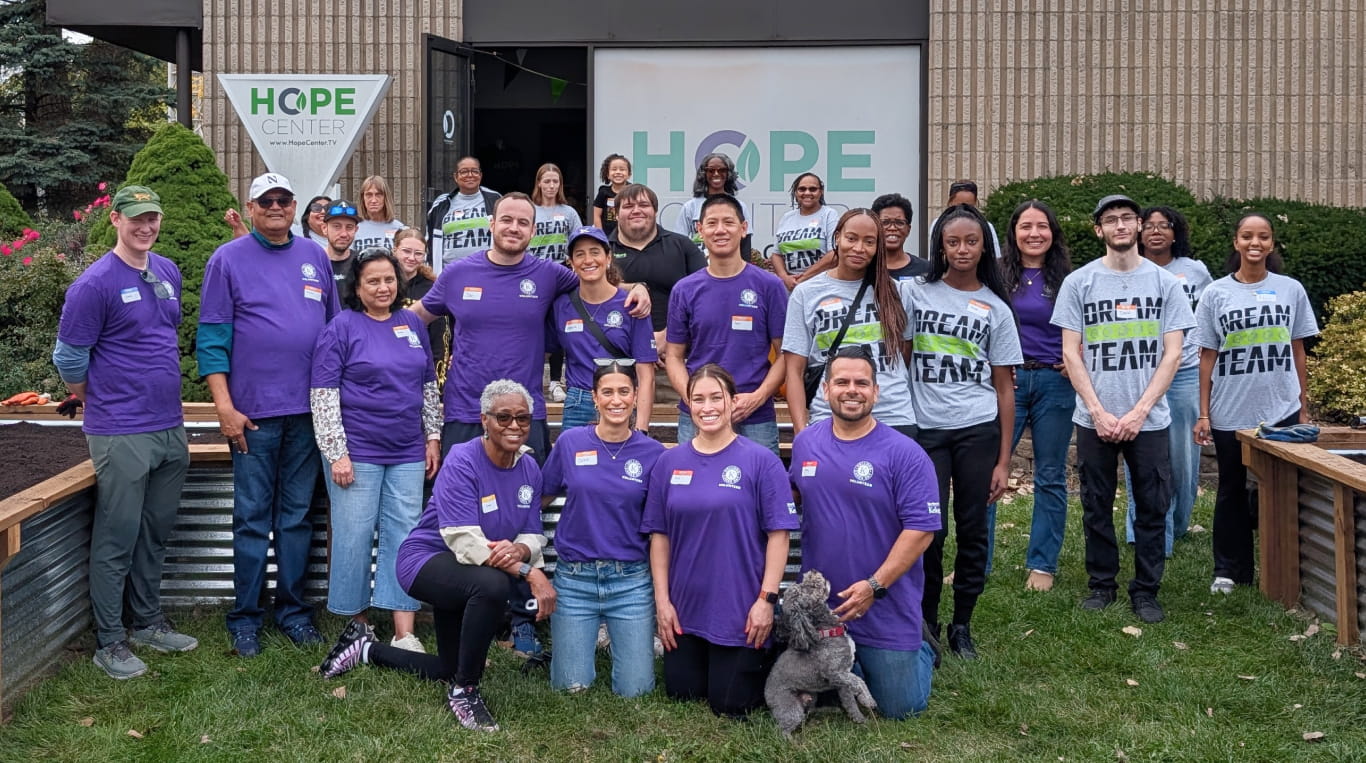 A group of adults wearing purple and grey t shirts standing outside on grass during a community service event