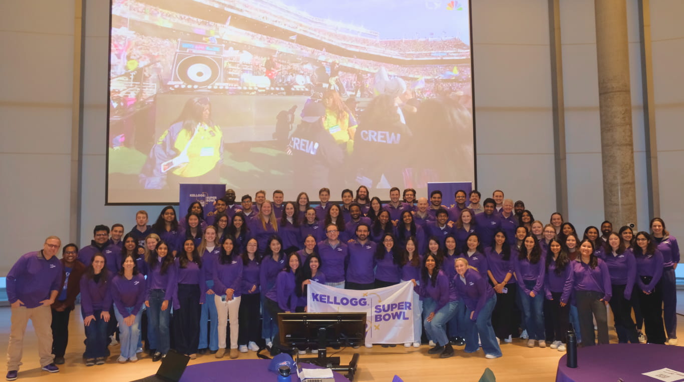 A group of men and women wearing purple shirts and standing in front of a project screen.