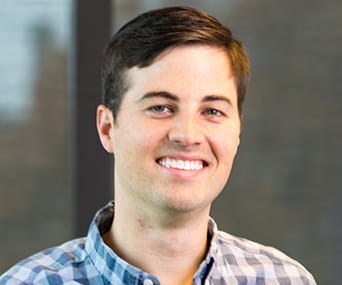 A white man wearing a collared dress shirt and smiling