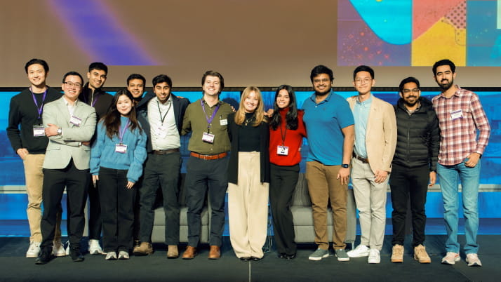 A group of 13 men and women standing on an elevated stage smiling