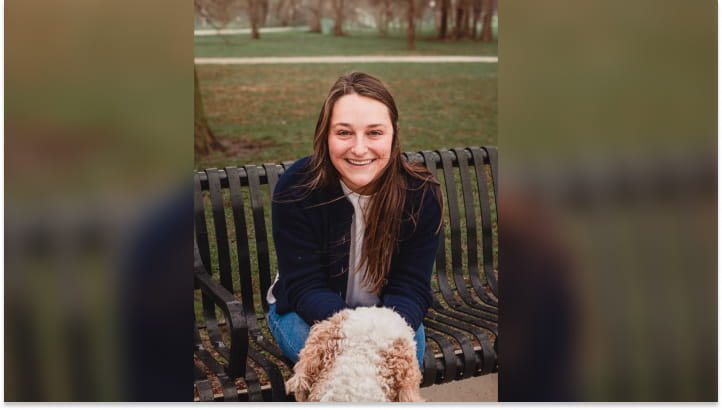 A woman with brown hair sitting on a bench with her dog