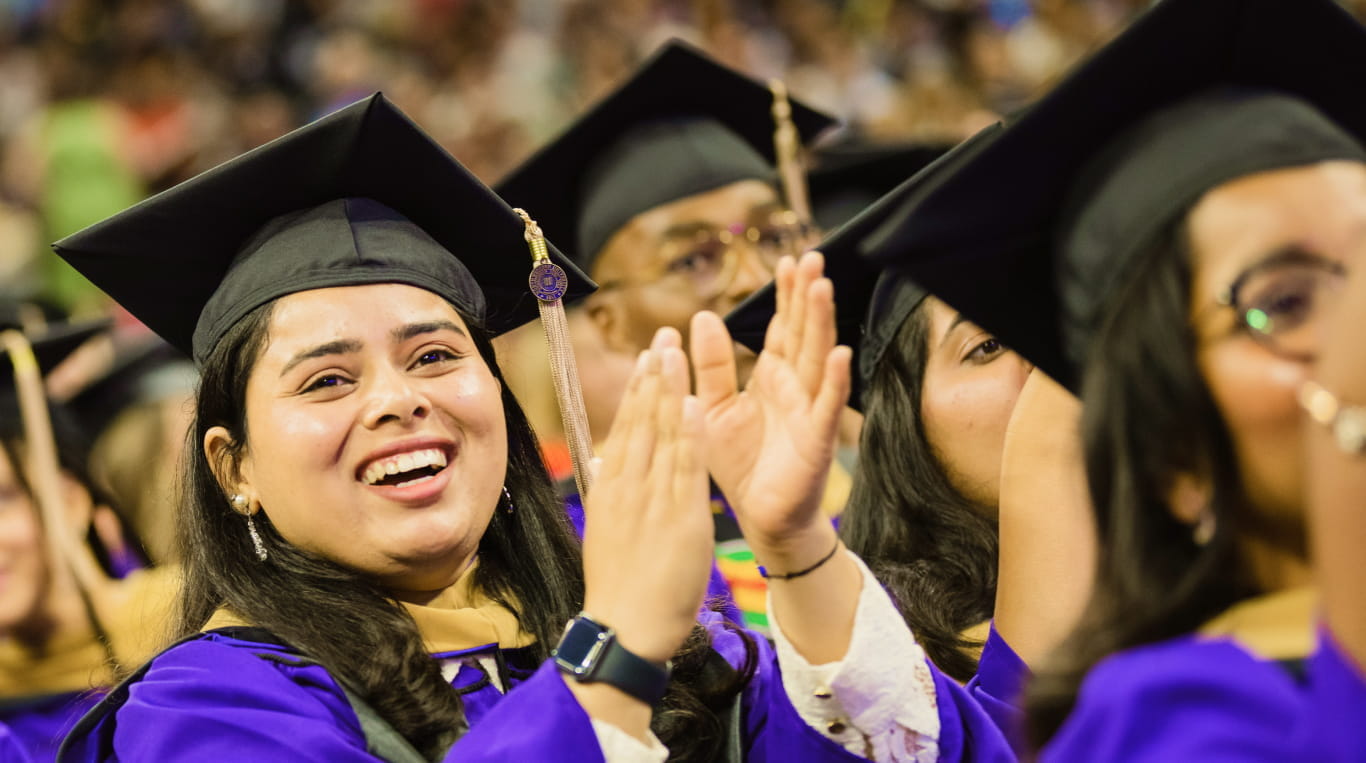 A woman wearing graduation regalia and clapping her hands