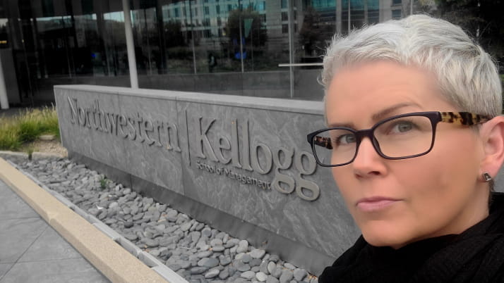 A woman with a platinum pixie cut wearing glasses in front of the Kellogg sign at the Global Hub