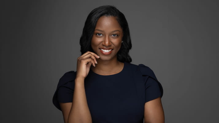 A dark skinned woman with her right hand resting near her mouth as she smiles