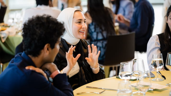 a woman sitting at a table and gesturing with her hands while talking with others