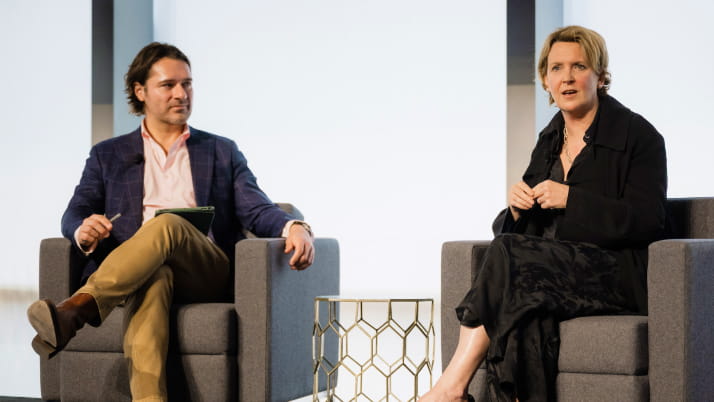 A man and a woman seated in chairs, as part of a panel discussion