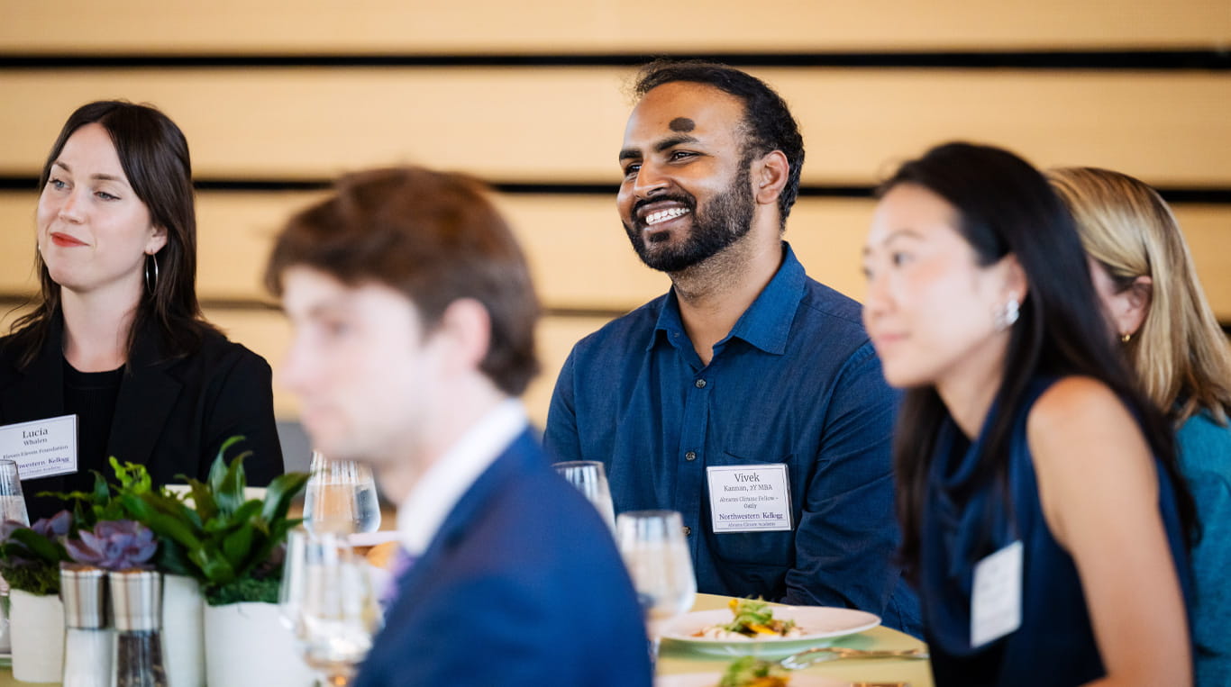 A dark-skinned man wearing a long-sleeve blue collared shirt seated near two other people.