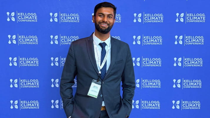 A dark-skinned man in a business suit with his hands in his pockets standing in front of a step and repeat.